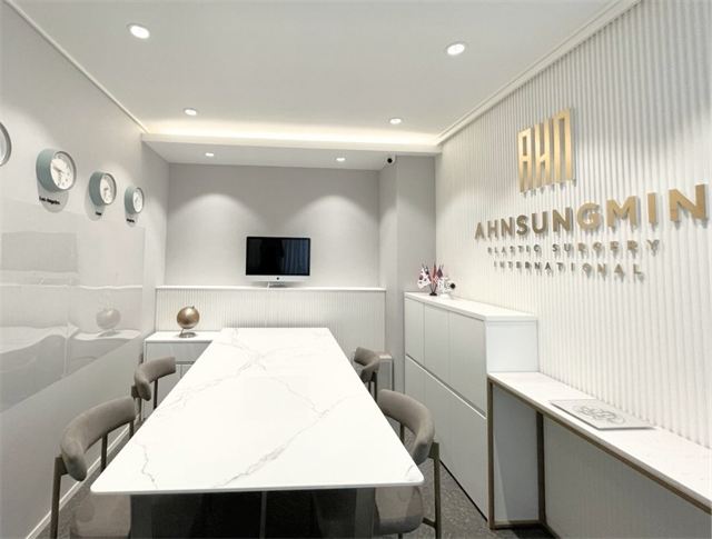 Consultation room with a long table and the clinic's logo wall at Ahn Sung Min Plastic Surgery