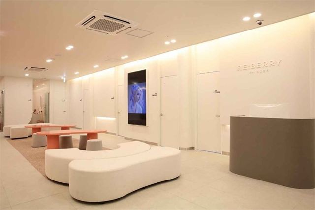 Waiting lounge with curved benches, coral tables and a RE:BERRY wall sign at Re:Berry Skin Clinic Yeongjong